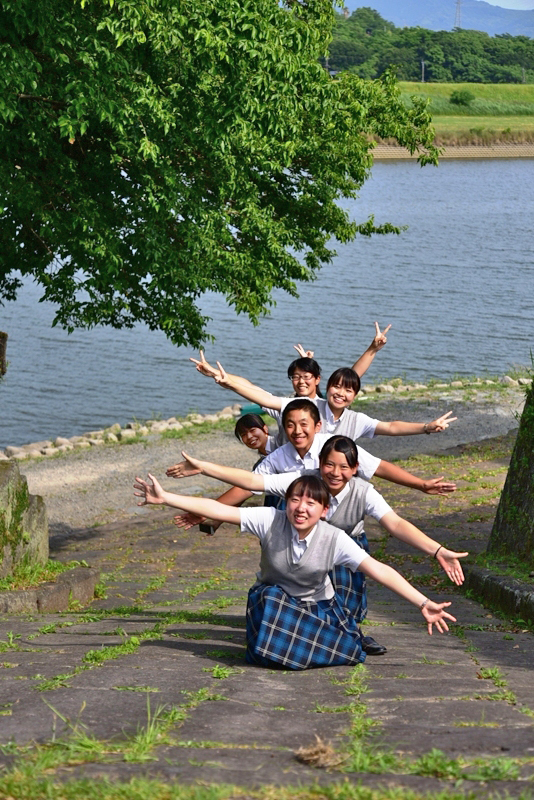 川の近くでポーズを取る学生達の写真