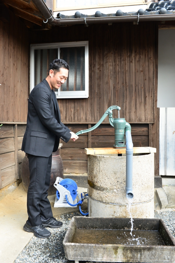 金栗さんの住家で手押しの水汲みを体験する勘九郎さんの写真
